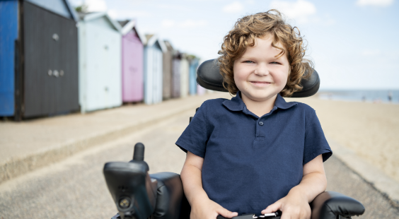 Image d’un jeune garçon souriant en fauteuil roulant sur une plage
